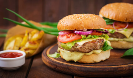 Big sandwich - hamburger with juicy beef burger, cheese, tomato,  and red onion on wooden background